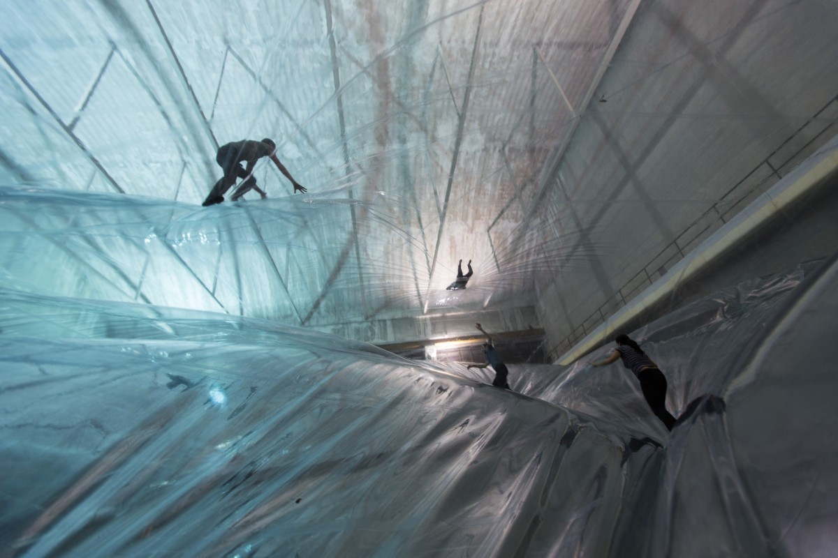 People climb on large inflated transparent sheets in an atrium space.