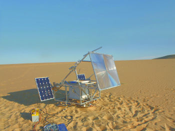 A large device with solar panels and a transparent lens in a sandy desert.