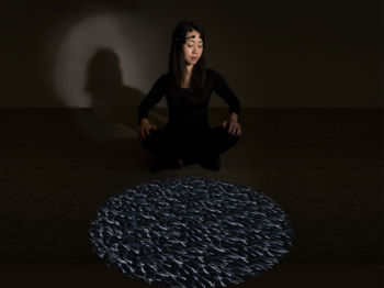 An artist sits in a dark room next to a spotlight projection.