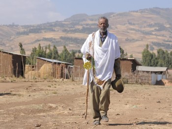 A man holding a sun-shaped lamp walks through a rural area