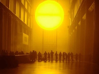 A group of people stands in a large hall illuminated by a large bright yellow orb