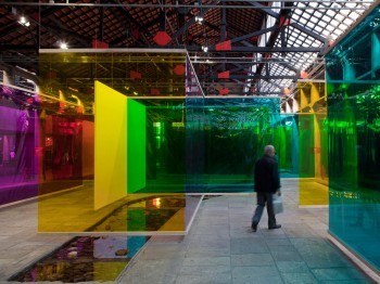 A person walks through a gallery with hanging tinted panels of glass