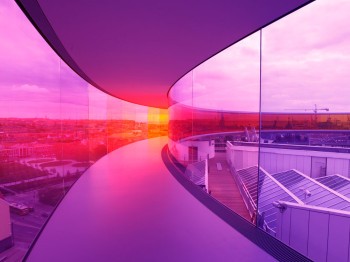 An elevated hallway with side walls made of pink and purple tinted glass