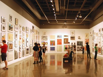 Students look at framed artworks in a gallery.