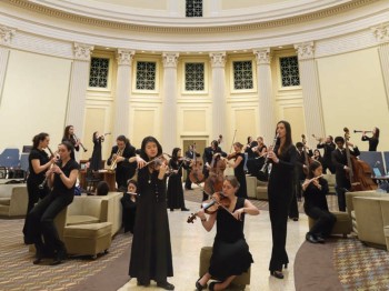 Many students play musical instruments in a reading room under a dome.