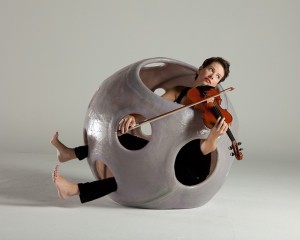 A woman plays violin from within a spherical sculpture with holes