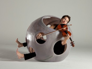 A woman plays violin from within a spherical sculpture with holes
