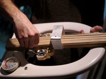 A hand plucks the strings on a musical instrument made of household objects.