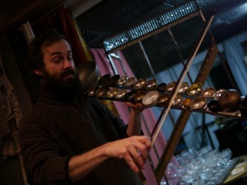 A man moves a violin bow across a series of metal discs.