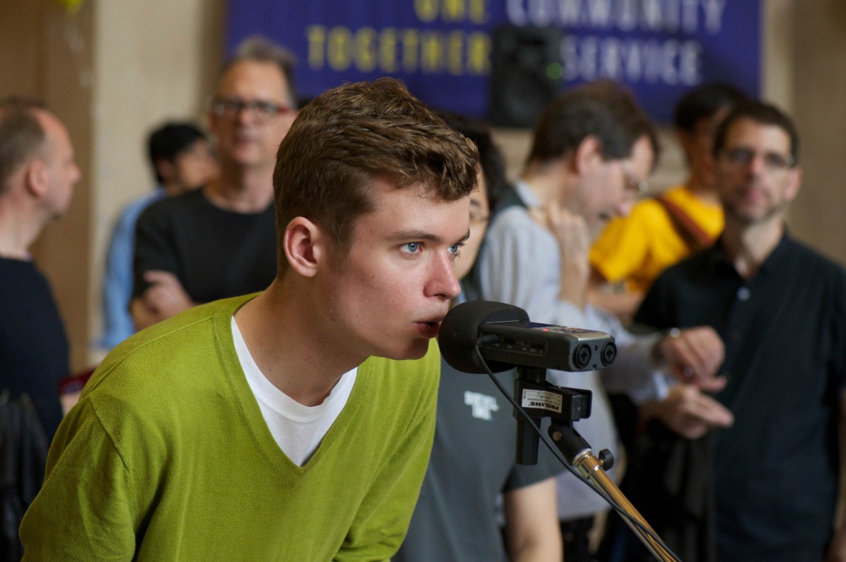 A student speaks into a microphone while others look on.