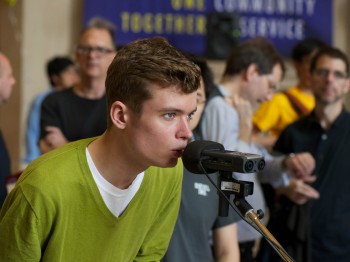 A student speaks into a microphone while others look on.