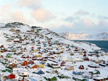 Many small colorful houses on a large snowy hill next to a bay.