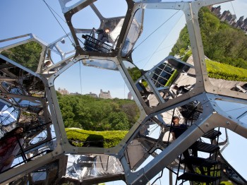 A structure made of interlocking geometric mirrors and panes of glass, reflecting buildings and trees.