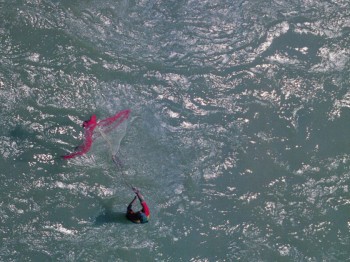 A photograph of a fisherman with a pink net in the ocean.