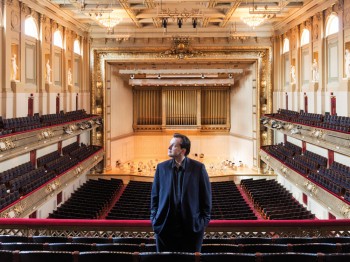 A man stands in the balcony seats of a large ornate concert hall.