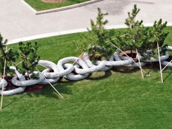 Large white stone sculpture in the shape of a chain, with small trees growing from within it.
