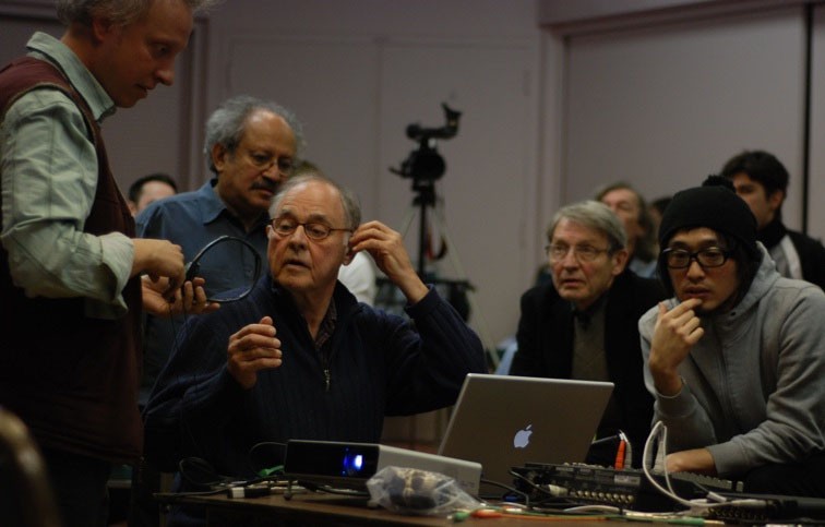 A group of people clustered around a table with laptops and audiovisual equipment.