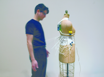 A person stands next to a mannequin wrapped in wires and thin rods.