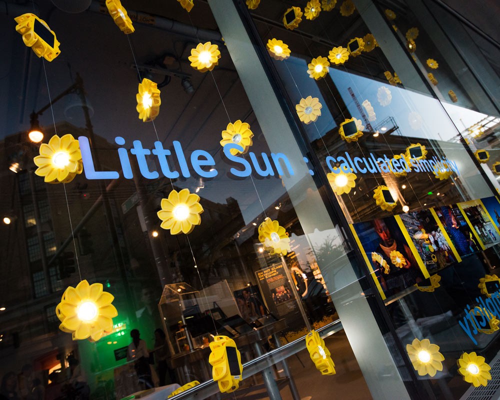 A window display showing hanging chains of sun-shaped lights reads "Little Sun: calculated simplicity"