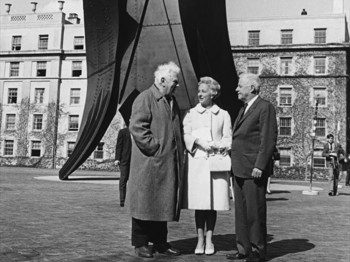 Black and white photo of three people standing in front of a tall metal outdoor sculpture
