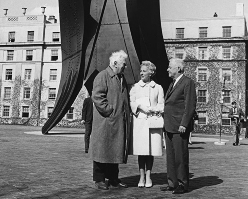 Black and white photo of three people standing in front of a tall metal outdoor sculpture