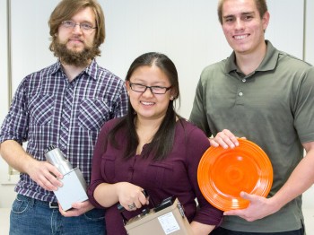 Three students pose holding metals and ceramic objects.