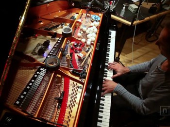 A man performs at a piano with many diverse objects on the strings