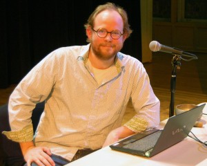 A man poses next to a microphone and a laptop.