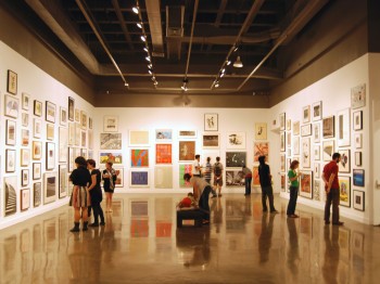 Visitors in a gallery with many framed paintings and photos on the walls.