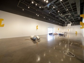 View of a contemporary art gallery installation with sculptures on the floor and walls.