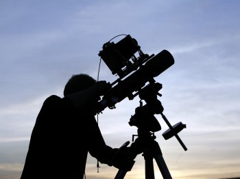 Silhouette of a man with a telescope against a blue sky.