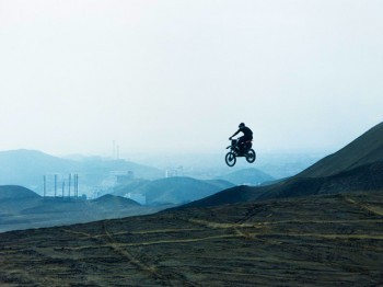 A motorcyclist flies off a jump on a hill.
