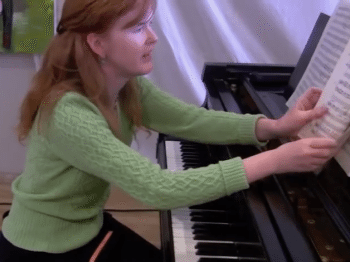 Video still of a woman turning pages of music at a piano