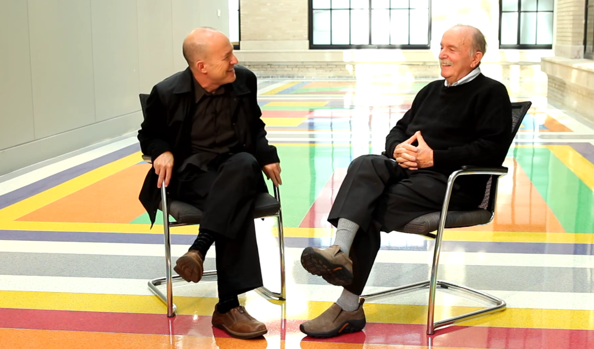 Alvin Lucier and Evan Ziporyn sit facing each other on the colorful and reflective MIT Sol LeWitt floor.