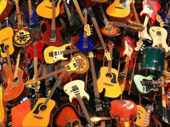 A pile of many different musical instruments, mostly guitars