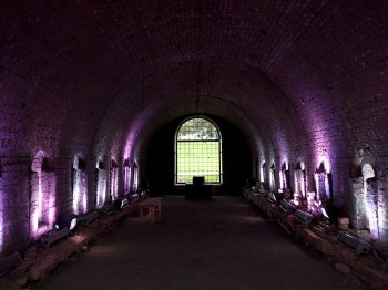 A brick tunnel illuminated by purple light, with a green field at the end.