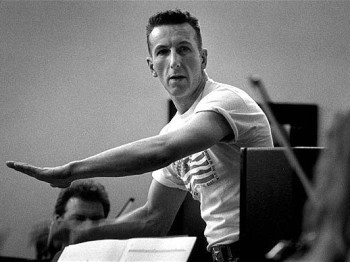 A conductor in a t-shirt rehearses with an orchestra.