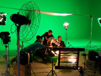 A group of people works with a technical setup and a tiger model in front of a green screen