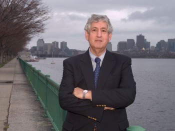 A man poses for a photo in front of the Charles River, with Boston in the background.