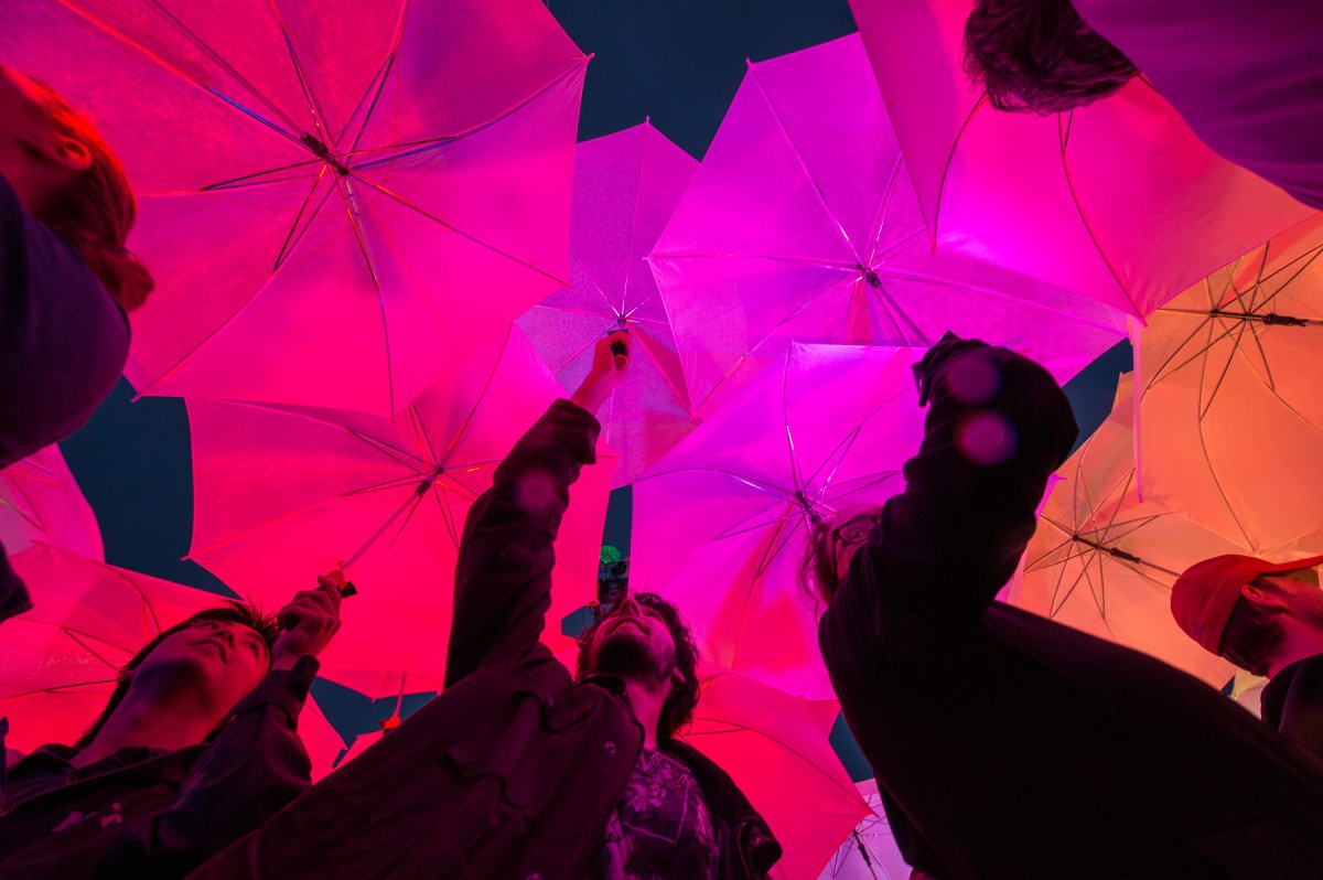 Students stand under multicolored umbrellas lit from within by LEDs.