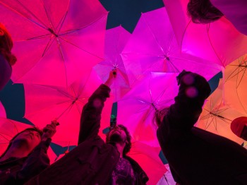 Students stand under multicolored umbrellas lit from within by LEDs.