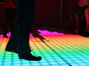 Feet dancing on a multicolored illuminated dance floor.