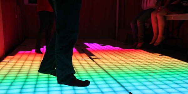 Feet dancing on a multicolored illuminated dance floor.