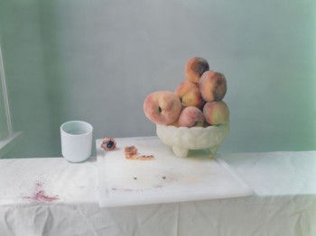 Image of a bowl of peaches on a cutting board next to a white mug.
