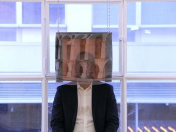 A man poses behind a semi-transparent hanging image of classical arches.