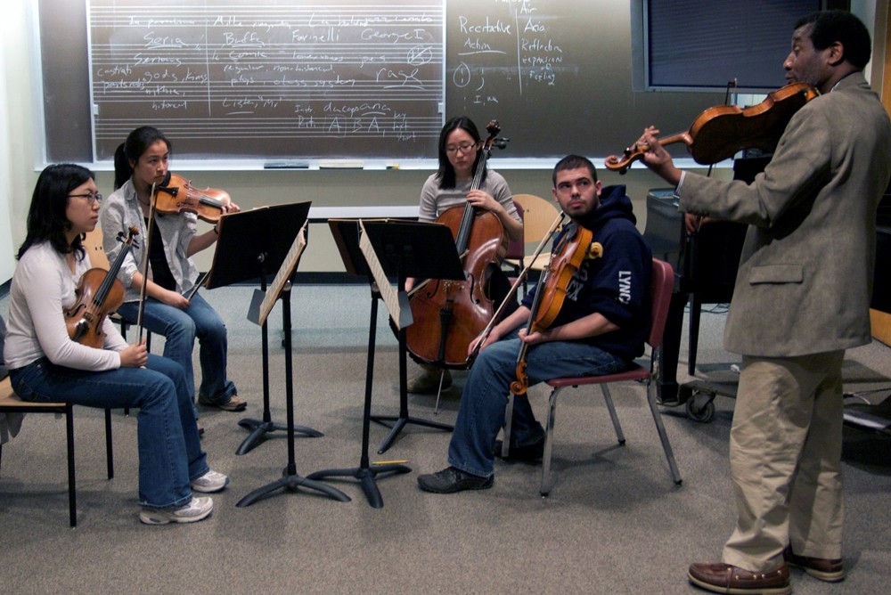 A string quartet rehearses with a professor in a classroom.