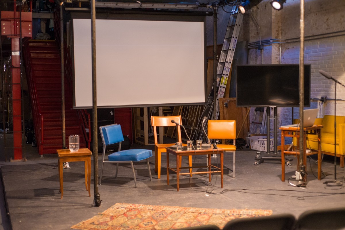 A stage set with tables, chairs, and screens.