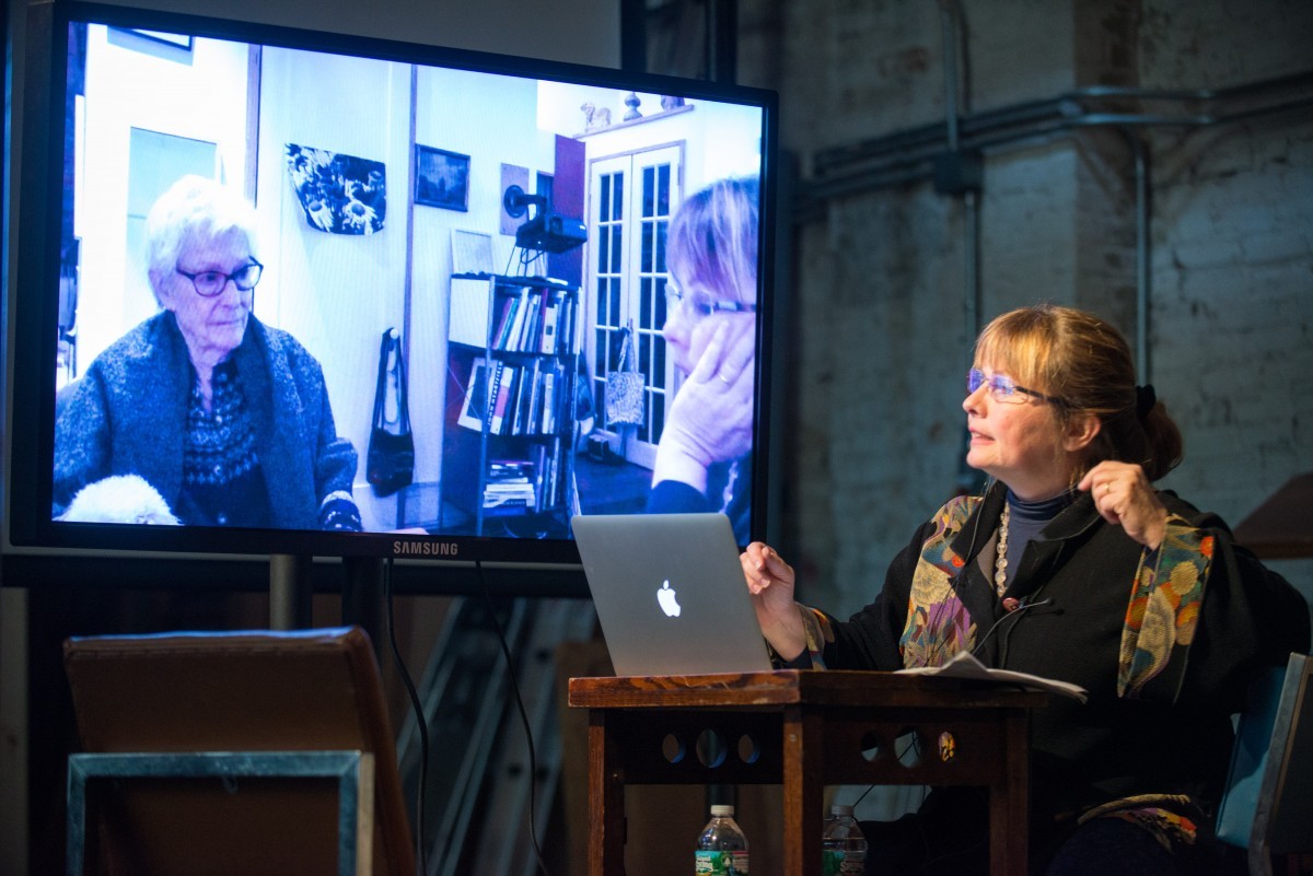 A woman with a laptop speaks next to a projection of herself and another woman.