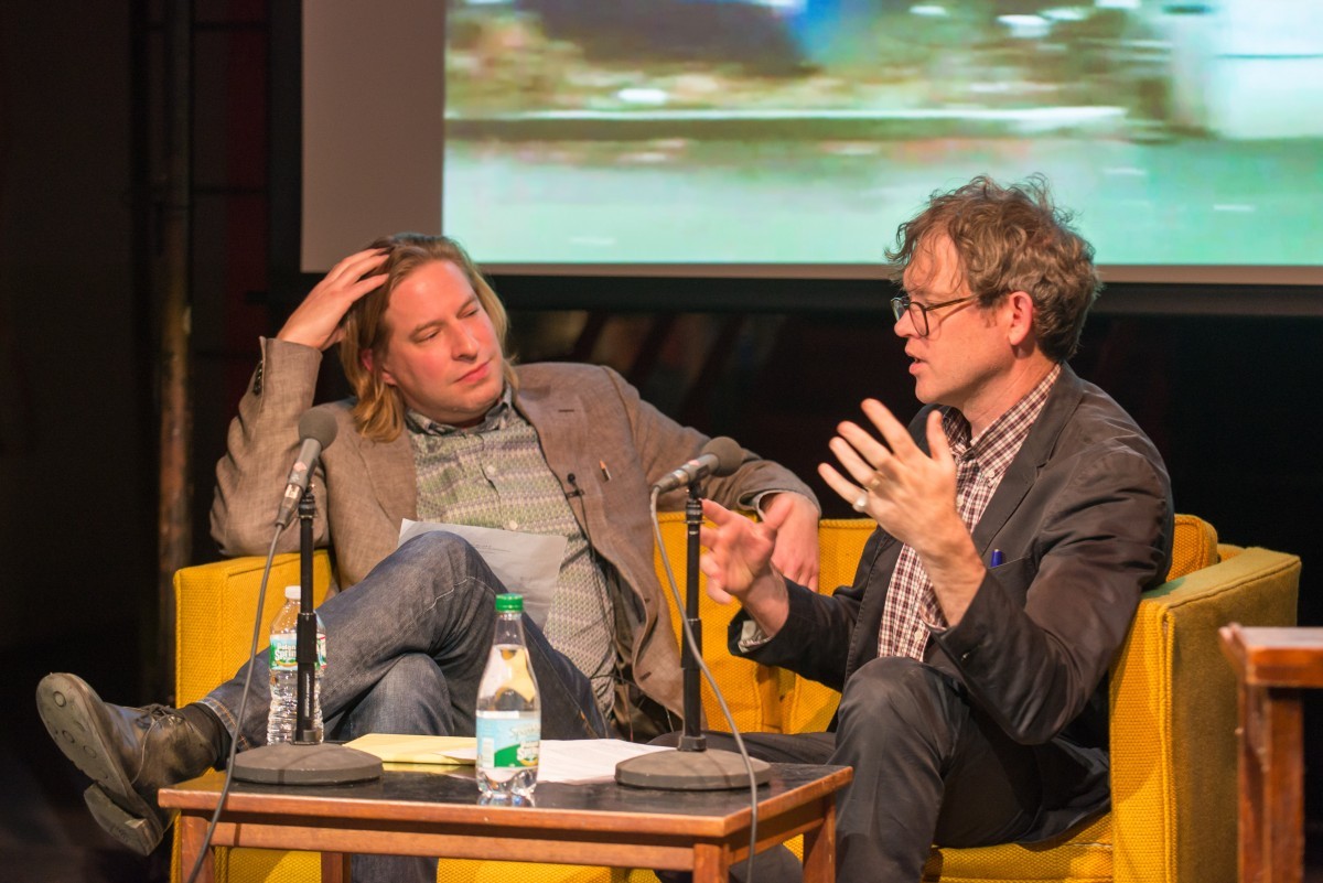 Two men in conversation on stage at a symposium.