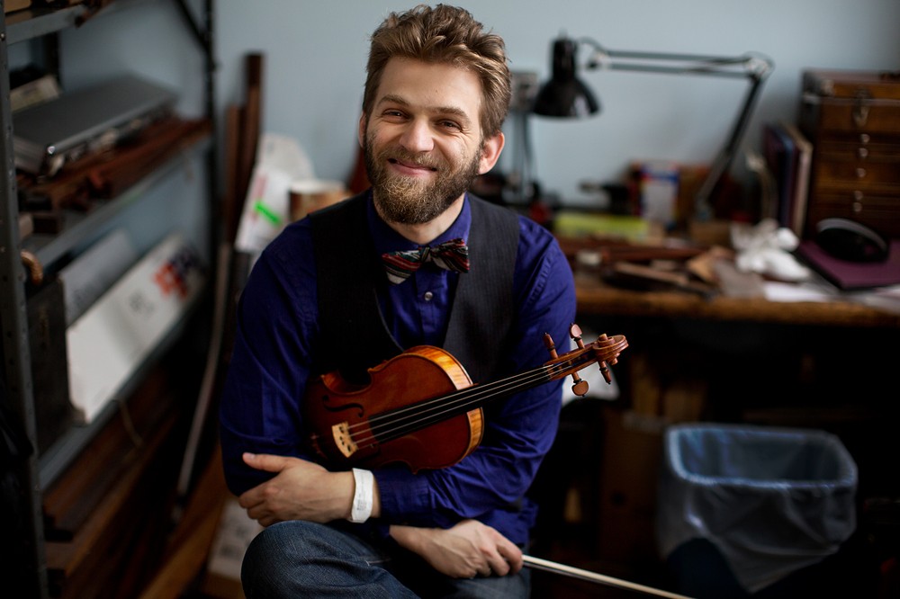 A man smiles holding a violin.